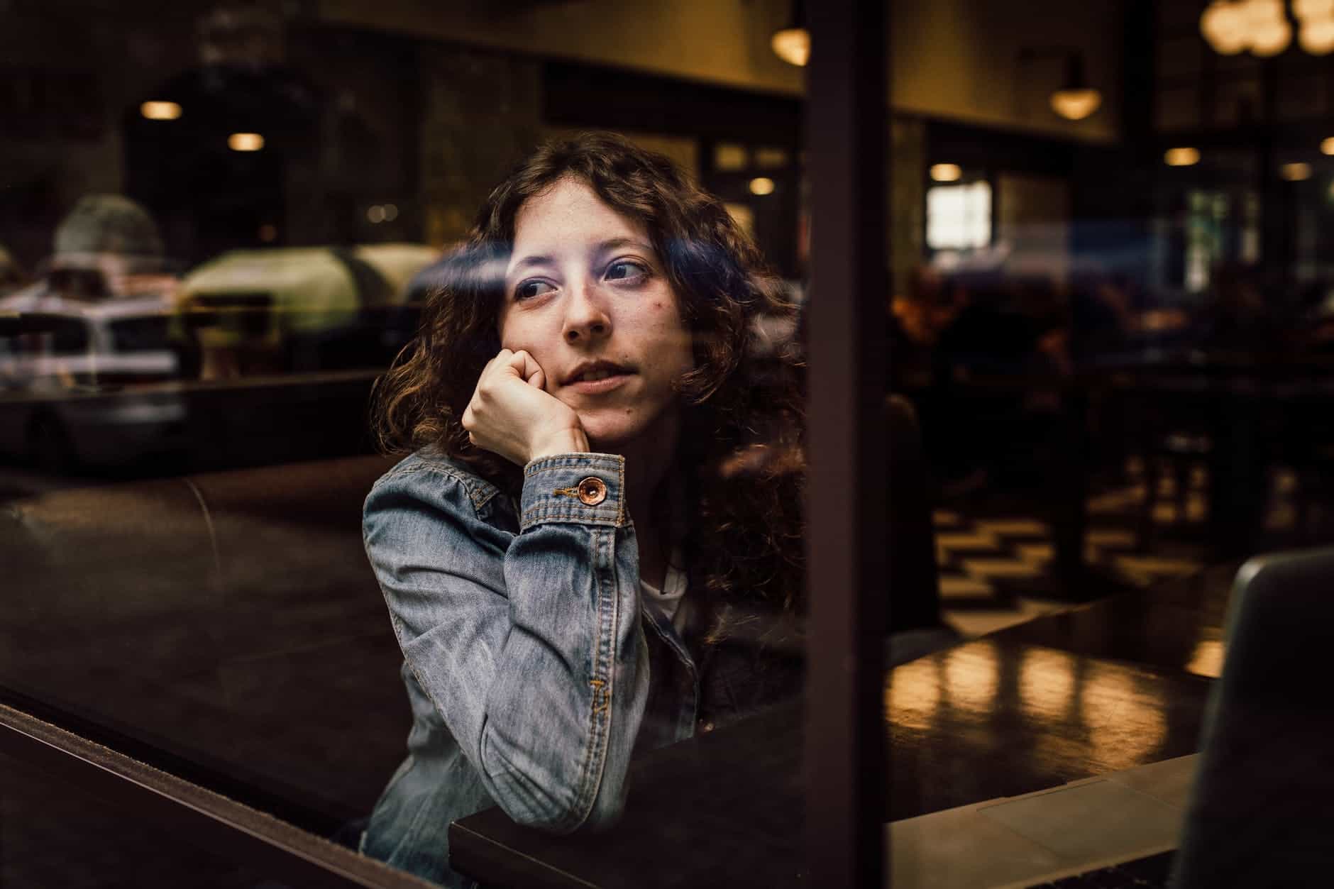 woman wearing blue denim jacket putting her right arm on her cheek